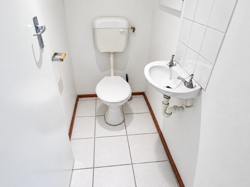 A compact powder room featuring a standard toilet and a wall-mounted basin with tiled splashback and ceramic floor tiles.