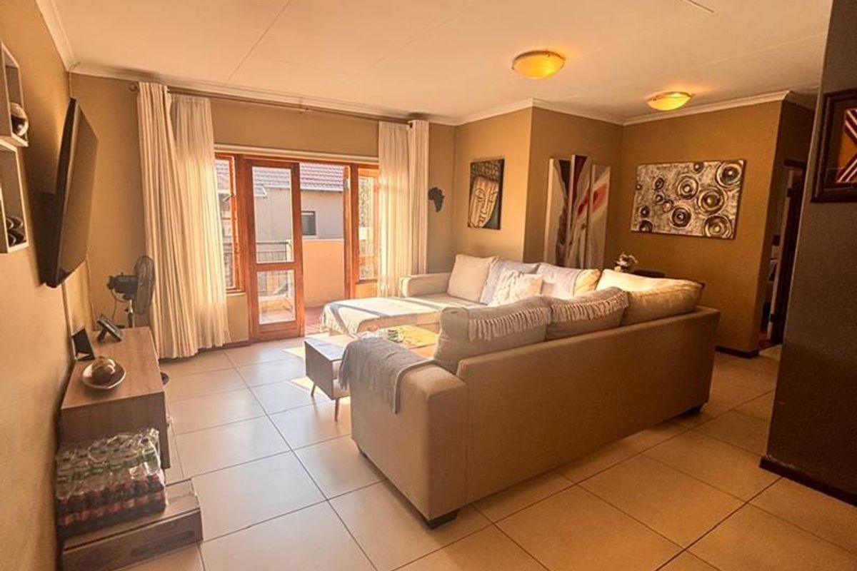 Spacious living room featuring large format floor tiles, warm wall tones, and direct access to an outdoor balcony through a sliding glass door.