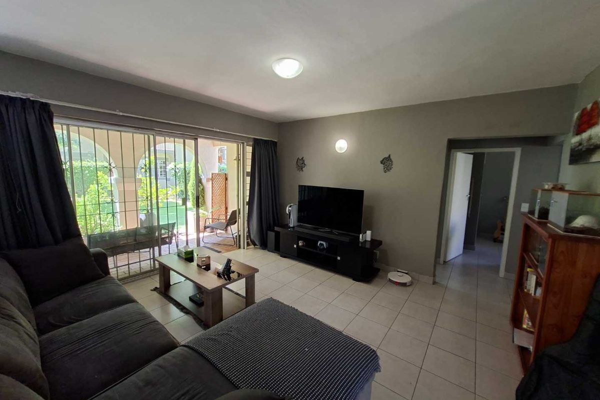 A living room featuring tiled flooring, neutral wall tones, and a large sliding glass door providing access to an outdoor patio area.