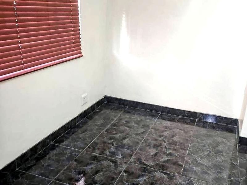 An empty room featuring dark marble-effect floor tiles, white walls, and fitted venetian blinds.