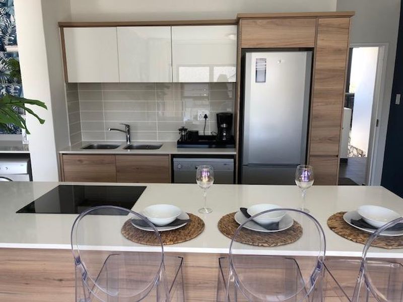 Modern kitchen featuring sleek wood-tone cabinetry, quartz countertops, a central island with an induction cooktop, and integrated appliances.