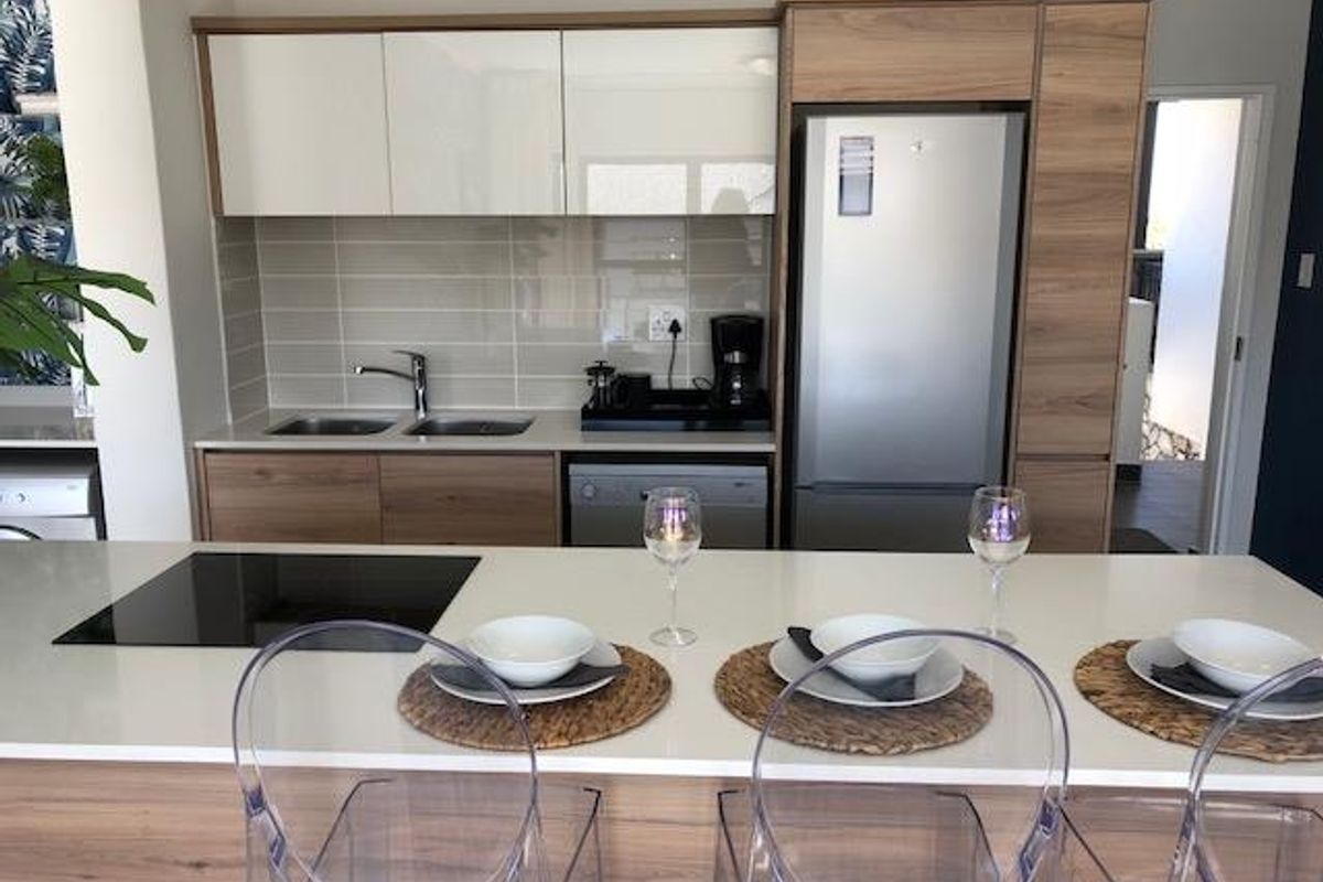 Modern kitchen featuring sleek wood-tone cabinetry, quartz countertops, a central island with an induction cooktop, and integrated appliances.