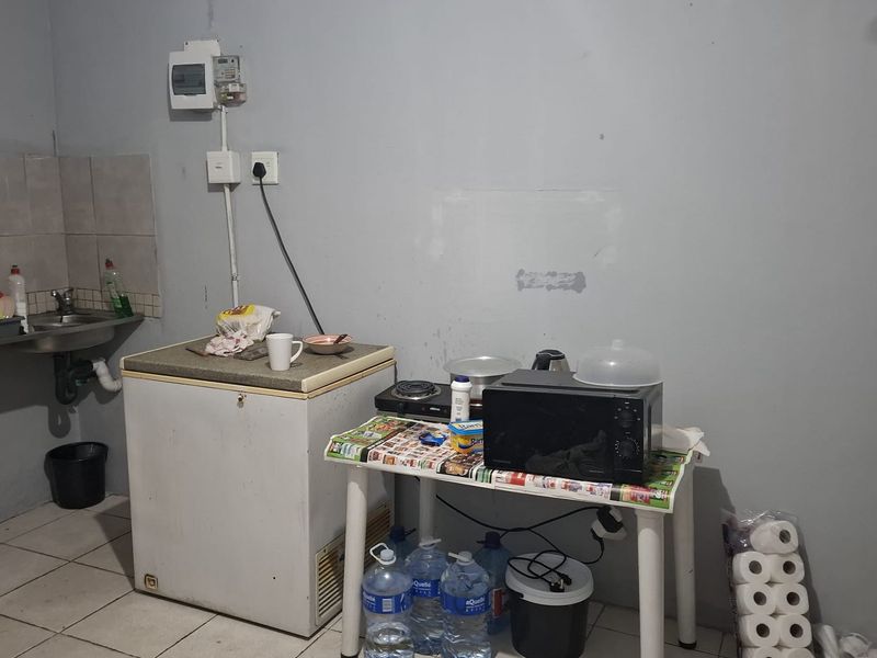 A basic kitchen area featuring a stainless steel sink, tiled flooring, and wall-mounted electrical distribution board, requiring significant cosmetic updates and improved finishes.