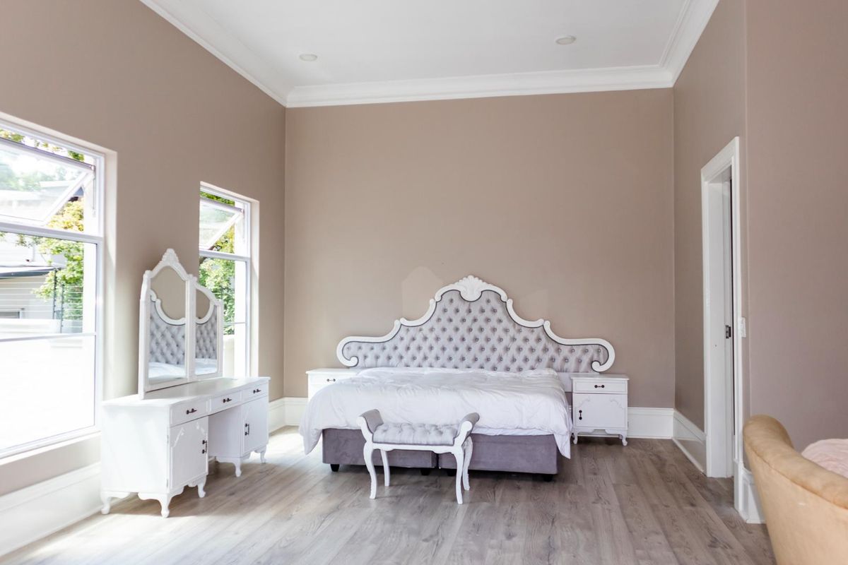 Spacious bedroom featuring neutral wall tones, timber laminate flooring, decorative cornice, and large windows providing ample natural light.