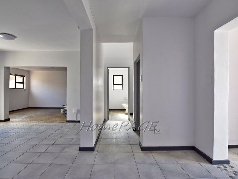 An open-plan living area featuring neutral ceramic floor tiles, white walls, and a clear view through to a secondary room and bathroom.