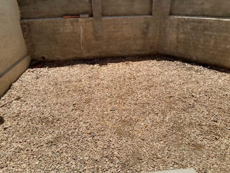 An unfinished rear outdoor area featuring a concrete boundary wall and a gravel-covered ground surface, offering potential for landscaping or patio development.