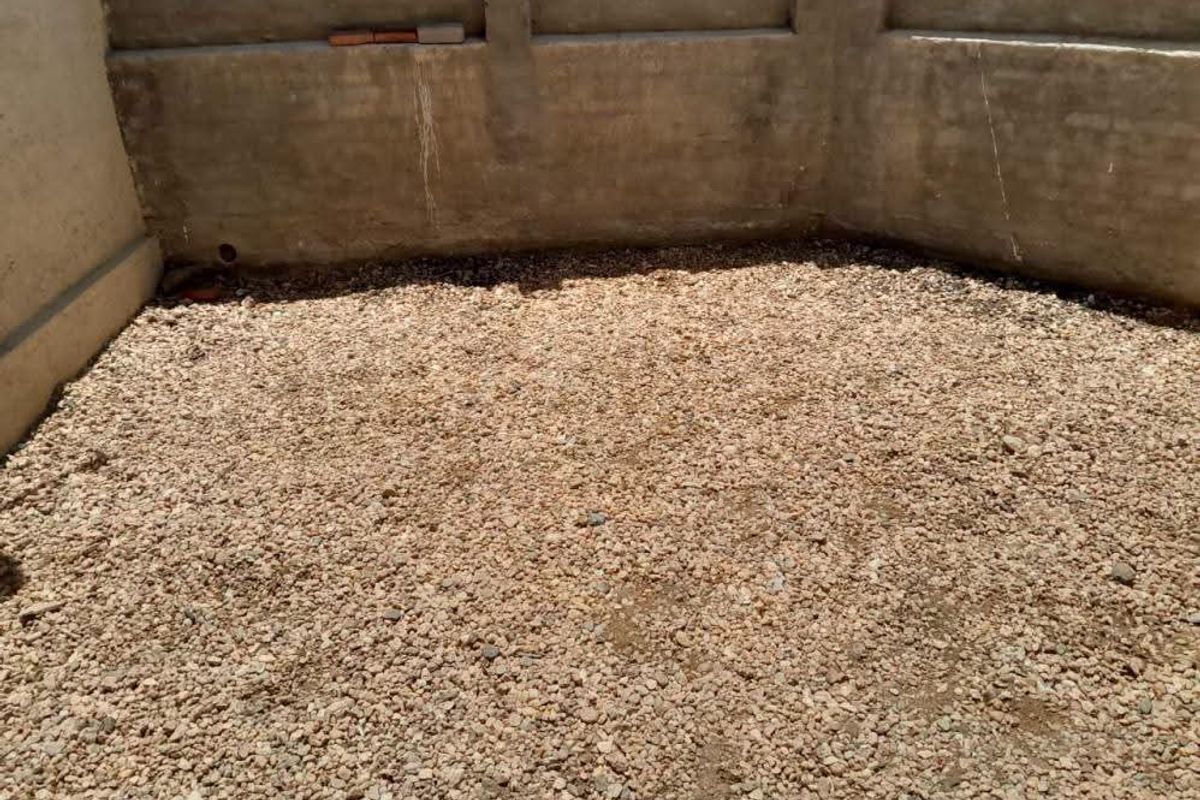 An unfinished rear outdoor area featuring a concrete boundary wall and a gravel-covered ground surface, offering potential for landscaping or patio development.
