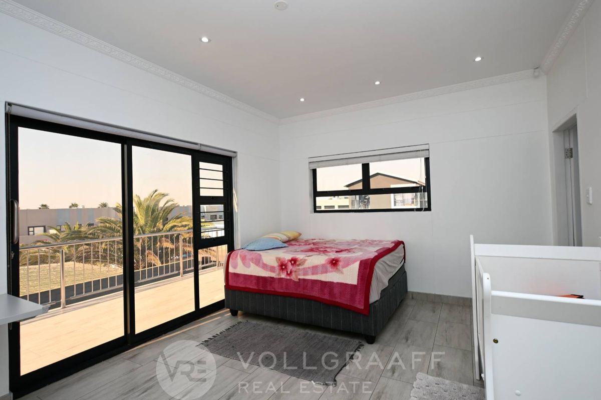 Bright bedroom featuring modern tiled flooring, recessed downlights, and large sliding glass doors opening to an outdoor balcony area.