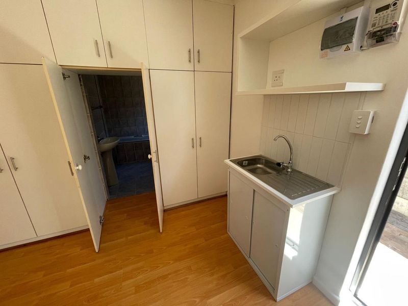A functional scullery or utility area featuring built-in cabinetry, a stainless steel sink, and laminate flooring, with direct access to an adjacent bathroom.