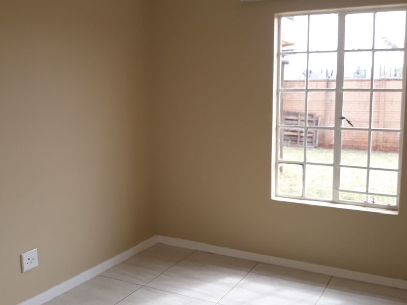 A clean, empty bedroom featuring neutral wall paint, tiled flooring, and a large grid-pattern window allowing natural light.