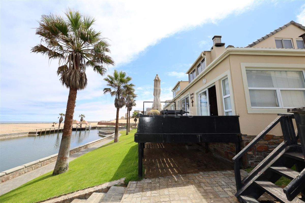 Rear exterior view of the townhouse featuring a raised timber deck, paved patio area, and direct access to the waterfront and beach.