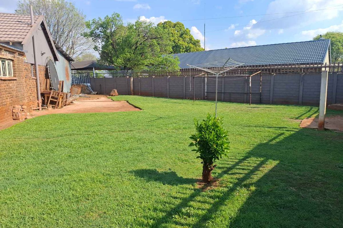 Spacious rear garden featuring a well-maintained lawn, enclosed by a secure precast concrete boundary wall and adjacent to the brick-clad house structure.