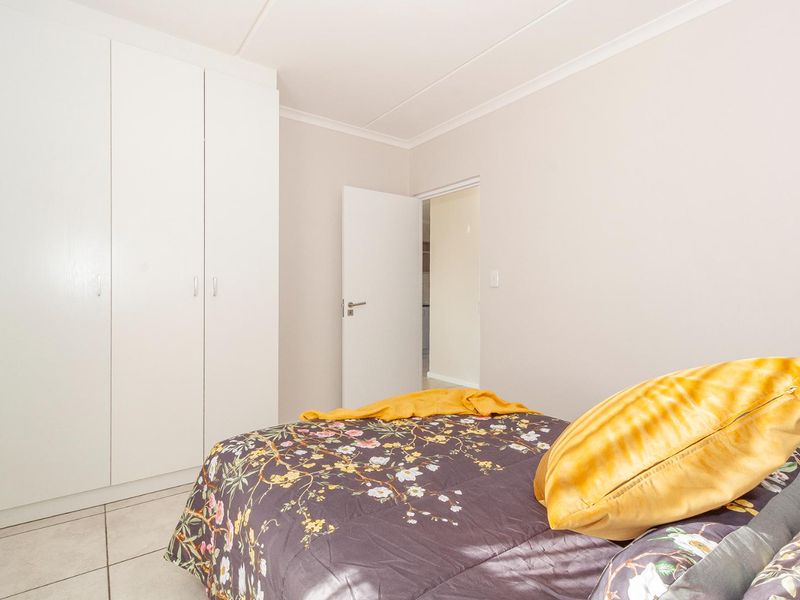 A bright bedroom featuring neutral walls, tiled flooring, and built-in white cupboards, offering a clean and functional living space.
