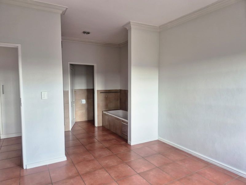An empty bathroom featuring tiled flooring, a built-in bathtub with tiled surround, and neutral wall finishes with crown molding.