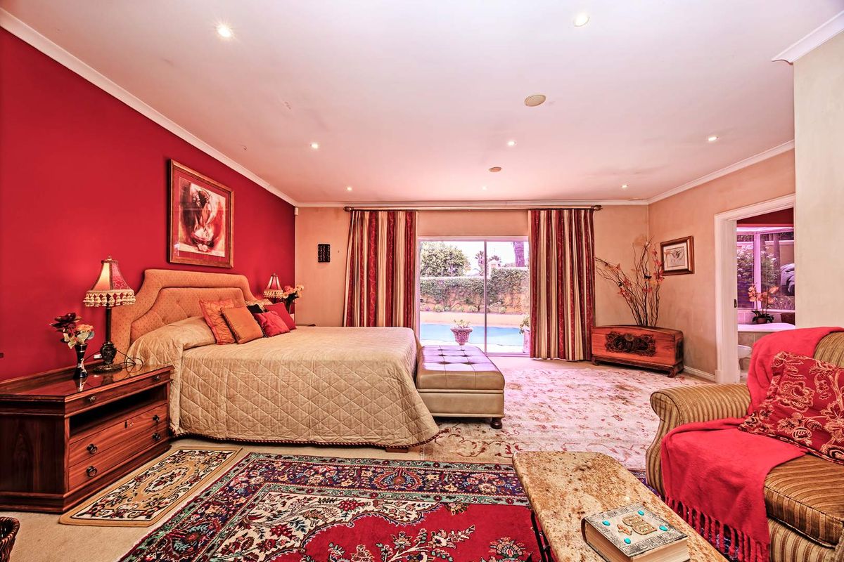 Spacious bedroom featuring a bold red accent wall, recessed lighting, and sliding glass doors providing direct access to the outdoor pool area.