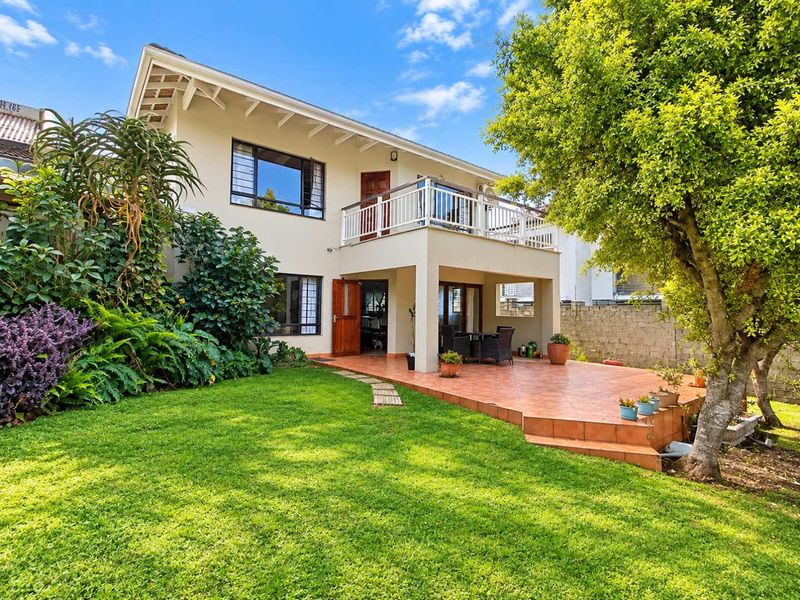 Rear view of the house featuring a tiled patio, an upper-level balcony with railing, and a well-maintained garden area.