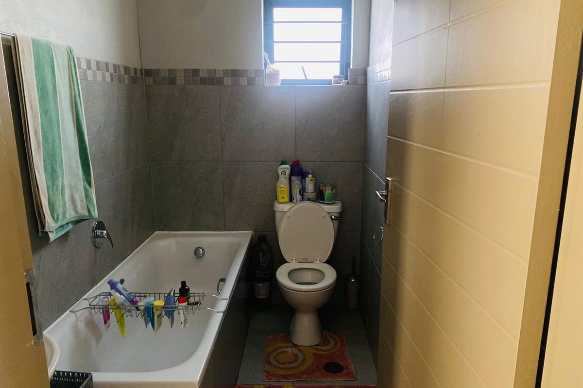 A compact bathroom featuring a built-in bathtub, a standard toilet, and neutral wall tiling with a decorative mosaic border.