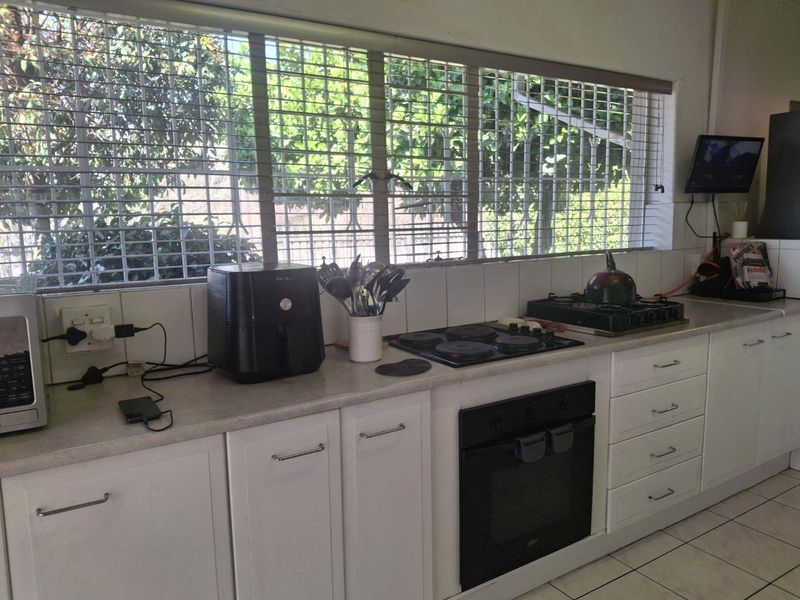 A functional kitchen featuring white cabinetry, laminate countertops, a built-in oven, and an electric hob, with large windows fitted with security bars.