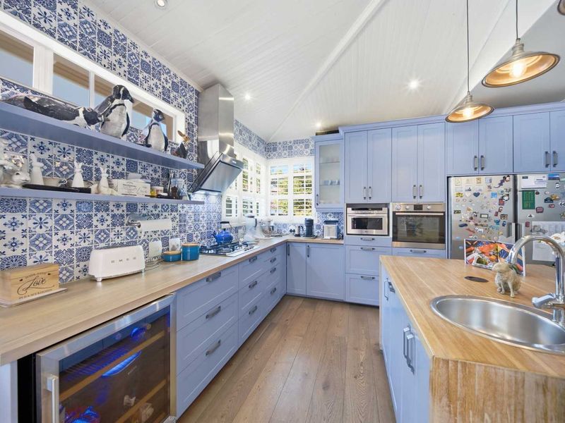 A well-appointed kitchen featuring light blue cabinetry, timber countertops, patterned tile splashbacks, and high-quality built-in appliances including a wine cooler.