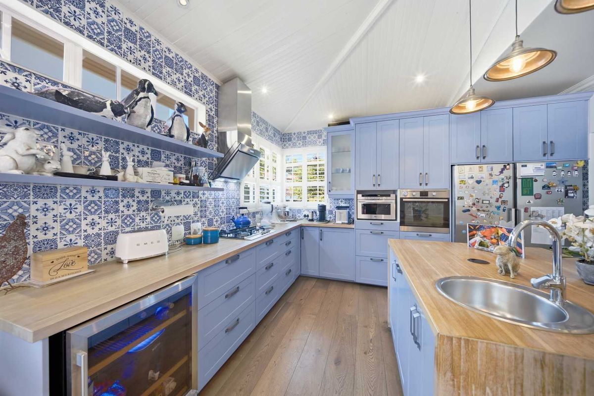 A well-appointed kitchen featuring light blue cabinetry, timber countertops, patterned tile splashbacks, and high-quality built-in appliances including a wine cooler.