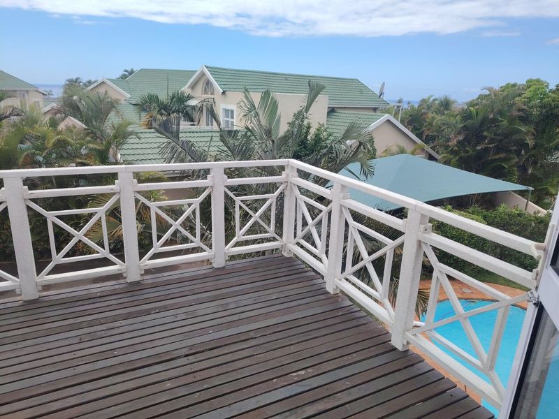An elevated timber balcony featuring a white balustrade railing, overlooking the complex garden and swimming pool area.