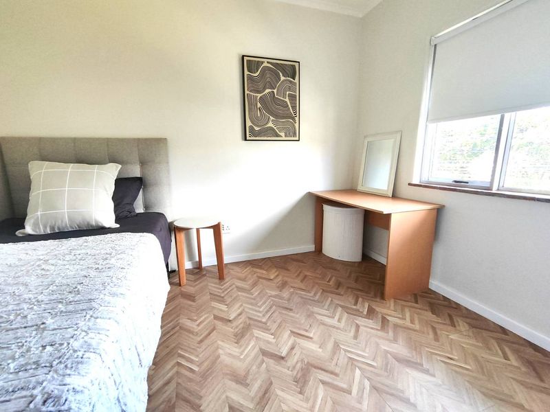 A well-maintained bedroom featuring modern herringbone timber flooring and a neutral color palette with a window fitted with a roller blind.