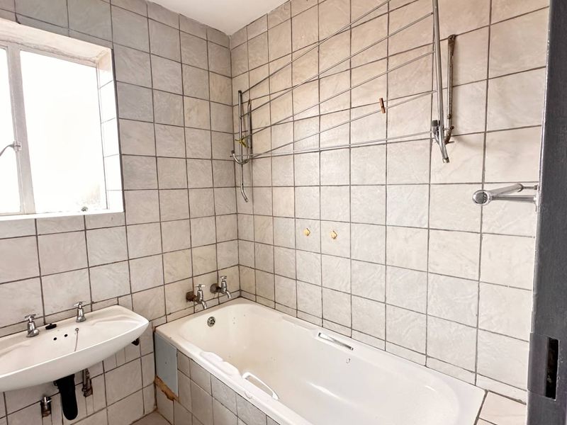A dated bathroom featuring a bathtub, wall-mounted basin, and full-height wall tiling, currently in need of cosmetic updates and repairs.