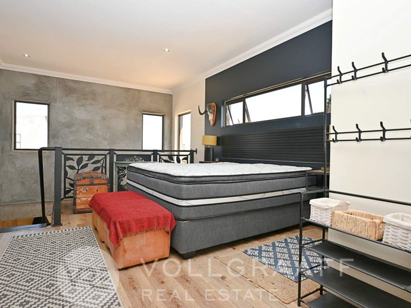 Spacious bedroom featuring timber flooring, a concrete feature wall, and a metal balustrade overlooking the lower level.