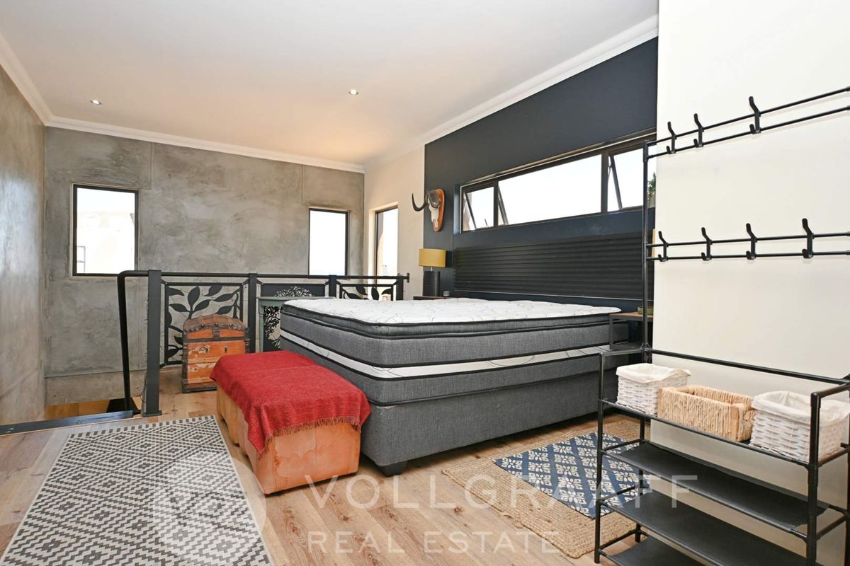Spacious bedroom featuring timber flooring, a concrete feature wall, and a metal balustrade overlooking the lower level.