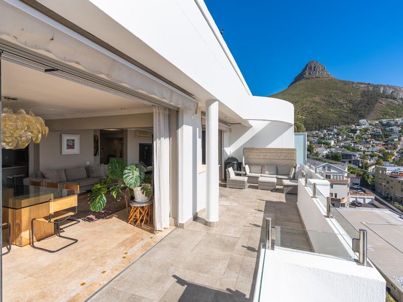Spacious balcony featuring a glass balustrade, tiled flooring, and a retractable awning, offering seamless indoor-outdoor flow and panoramic mountain and city views.