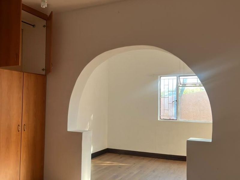 A vacant bedroom featuring built-in wooden cupboards, laminate flooring, and a distinctive arched doorway leading to an adjoining space.