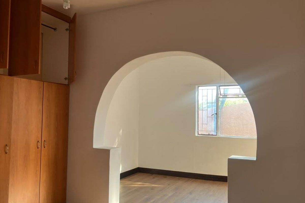 A vacant bedroom featuring built-in wooden cupboards, laminate flooring, and a distinctive arched doorway leading to an adjoining space.
