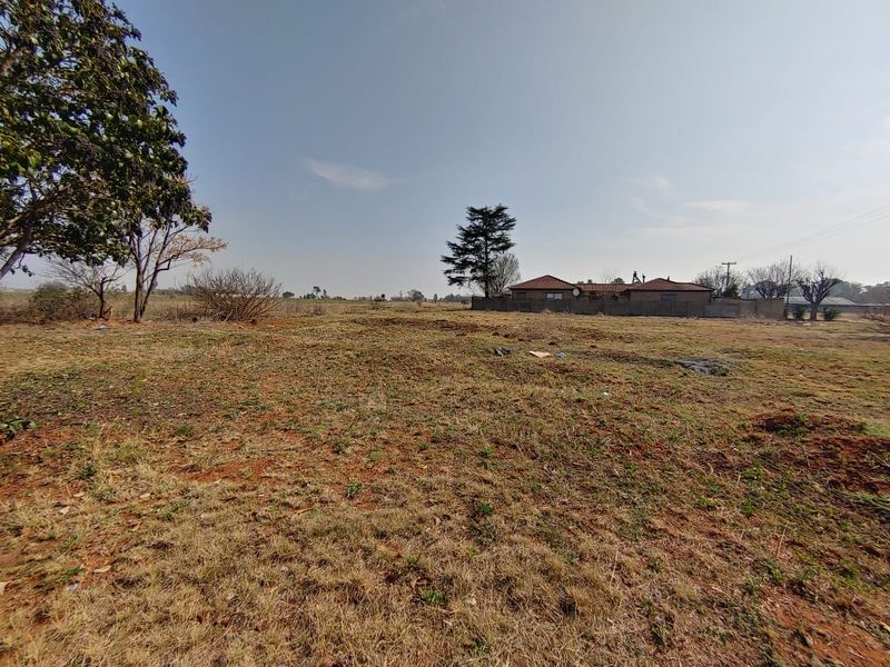 A wide-angle view of a vacant residential plot featuring natural grass cover and a boundary wall in the background.