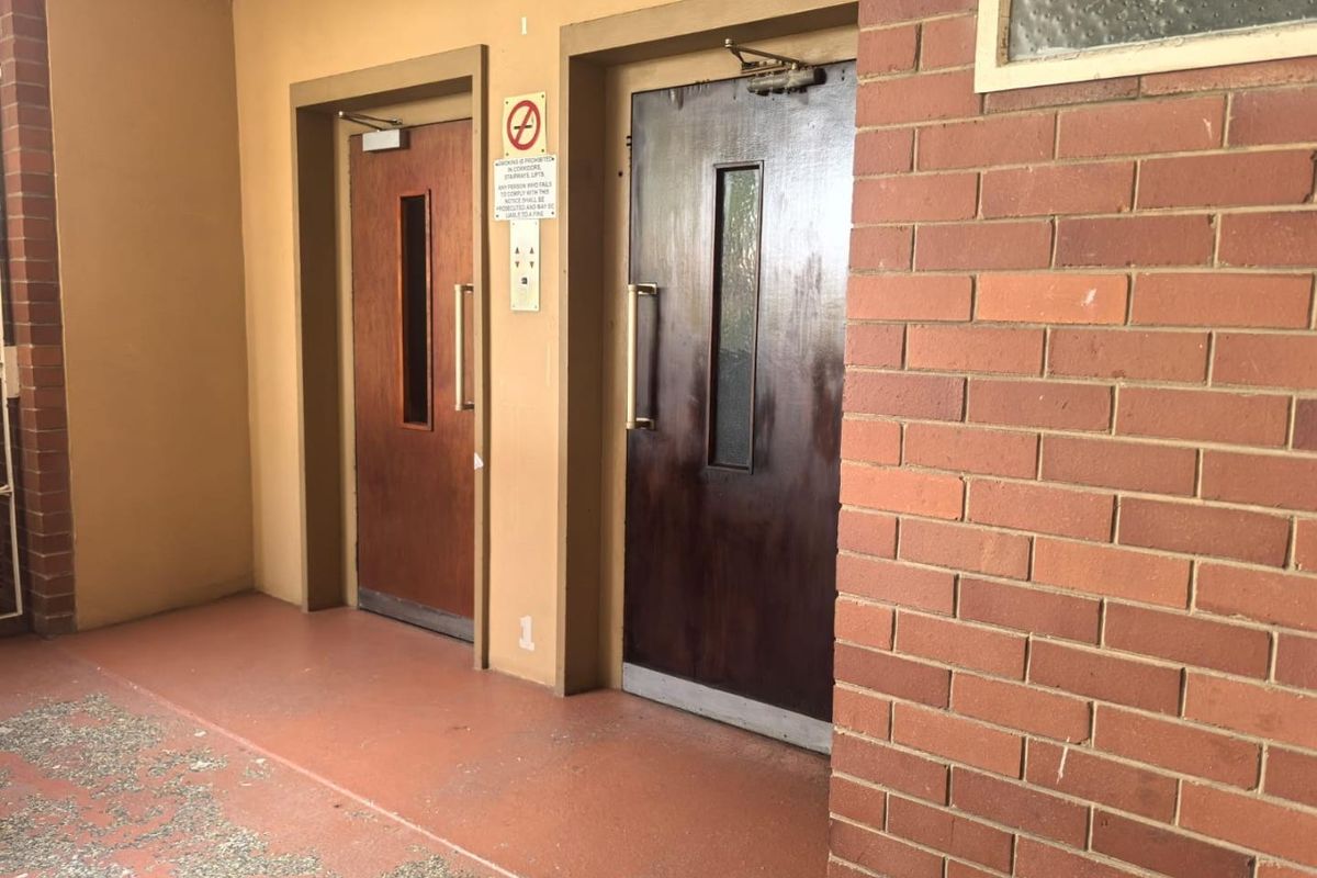 Entrance area featuring two solid core fire doors with door closers, set against a brick and painted wall facade.