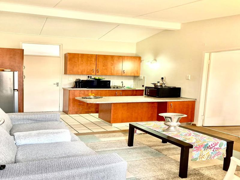 Open-plan living area featuring a functional kitchen with wood-finish cabinetry, laminate countertops, and tiled flooring, seamlessly connected to the lounge space.