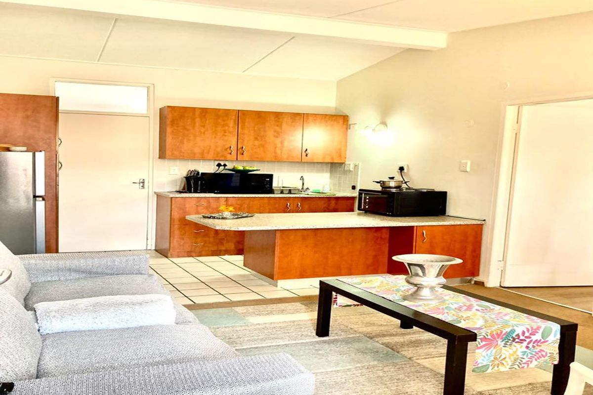 Open-plan living area featuring a functional kitchen with wood-finish cabinetry, laminate countertops, and tiled flooring, seamlessly connected to the lounge space.