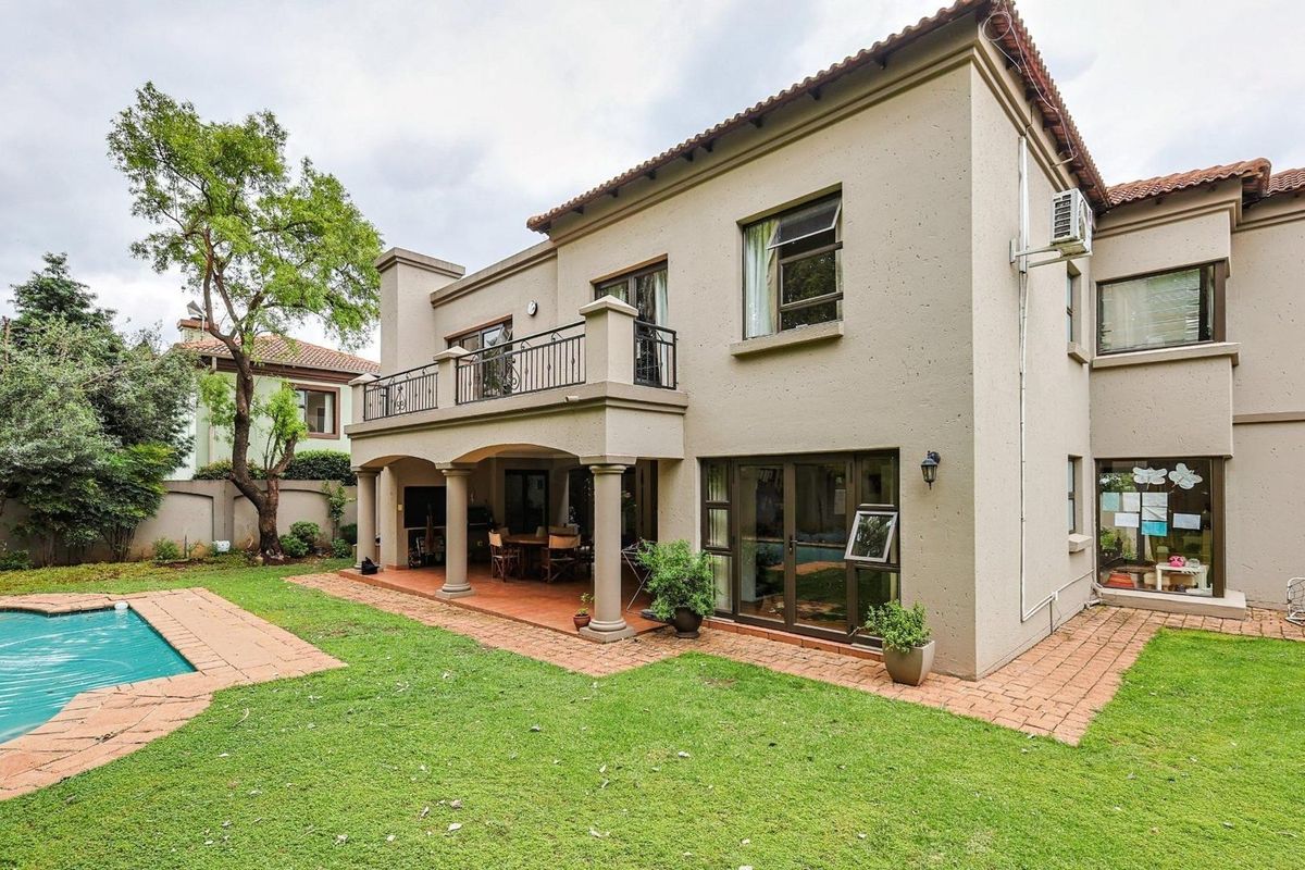 Rear view of a two-story house featuring a covered patio, upper balcony with wrought iron railing, swimming pool, and landscaped garden area.