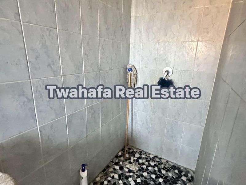 A small shower enclosure featuring tiled walls and a mosaic-style tiled floor, currently showing signs of wear and damage to the floor tiling.