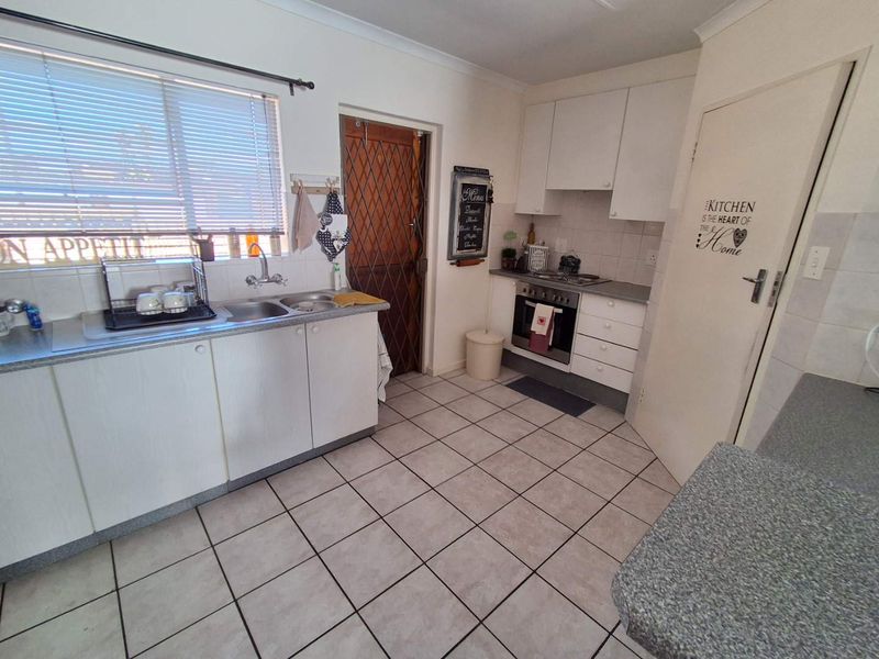 A functional kitchen featuring laminate cabinetry, a double basin sink, built-in oven, hob, and tiled flooring with a rear security door.