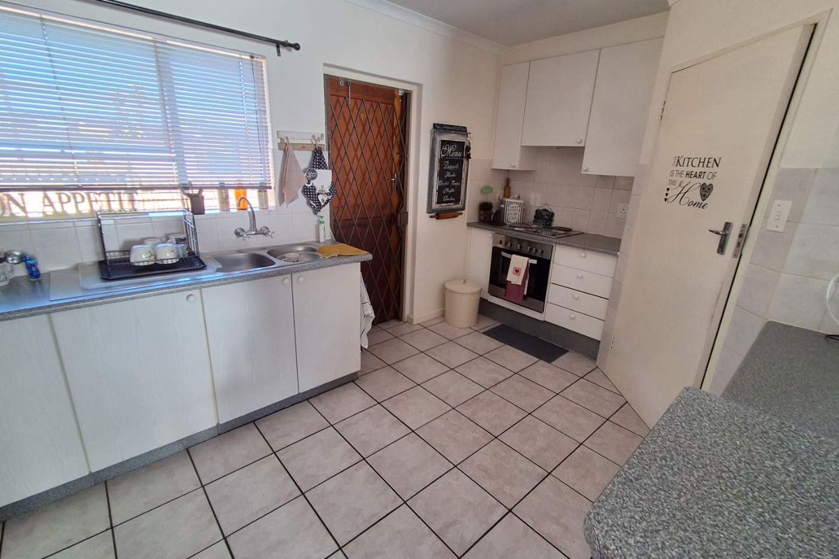 A functional kitchen featuring laminate cabinetry, a double basin sink, built-in oven, hob, and tiled flooring with a rear security door.