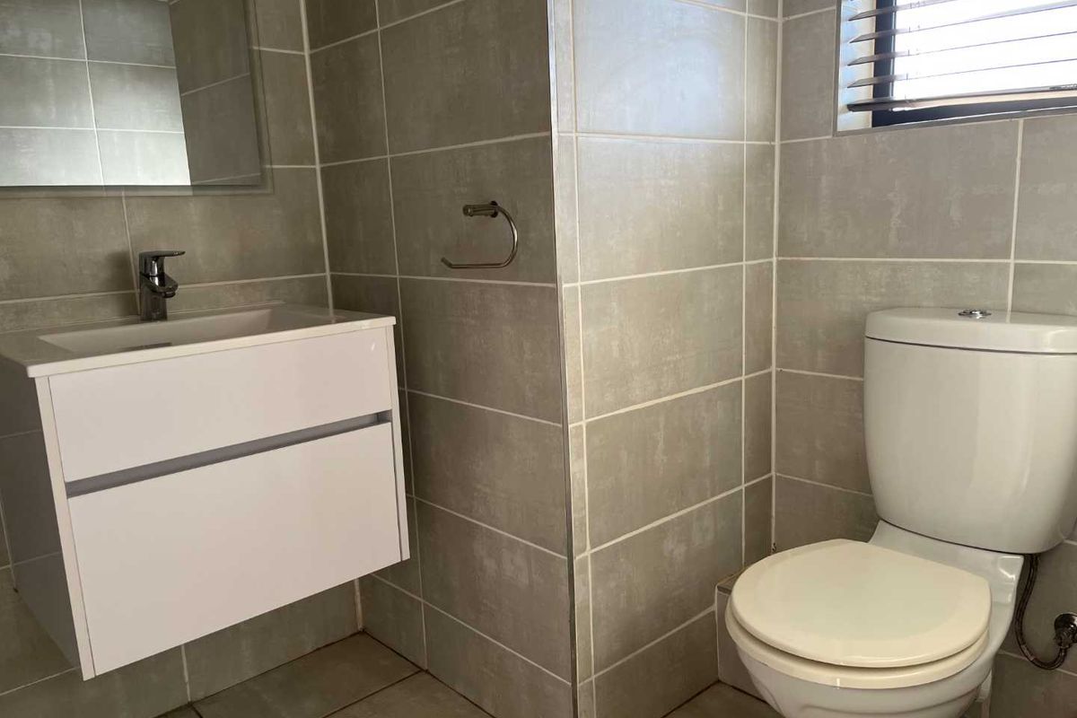 A clean, modern bathroom featuring neutral wall tiles, a wall-mounted vanity with a basin, and a standard toilet.