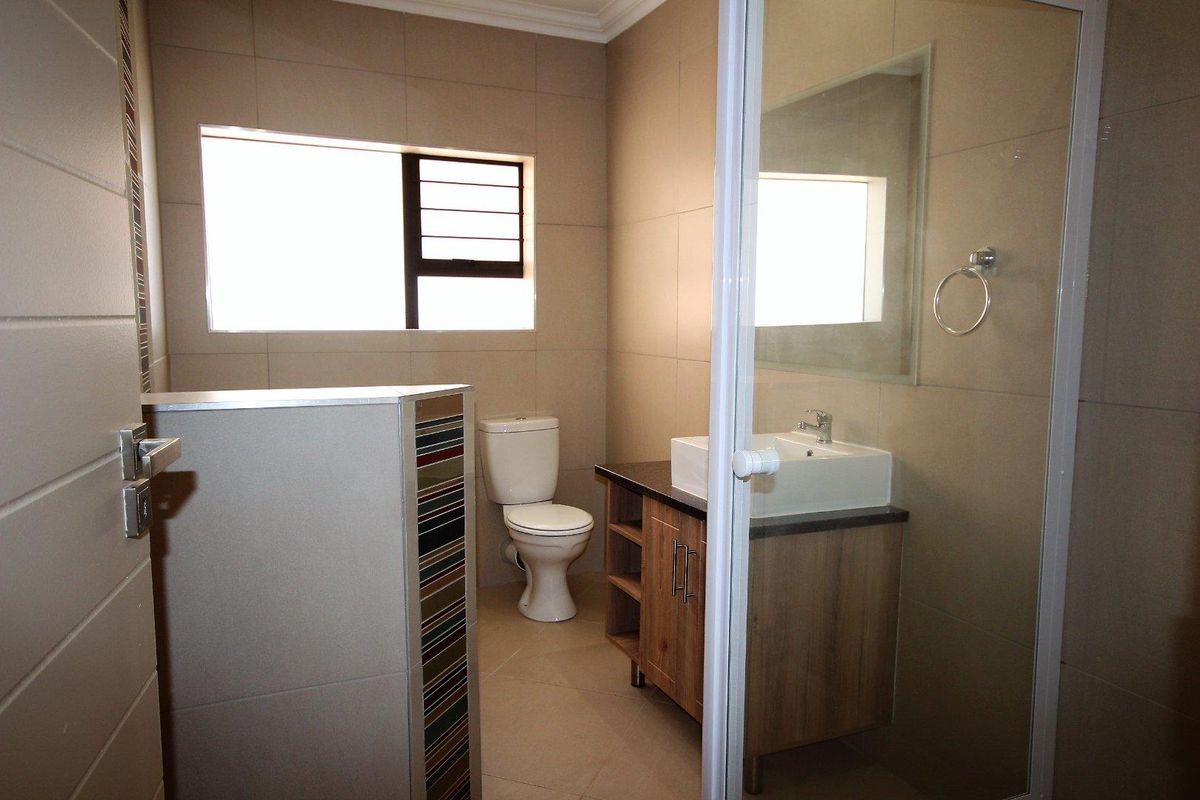 A modern bathroom featuring a vessel sink vanity, a toilet, and a glass-enclosed shower with neutral wall and floor tiling.