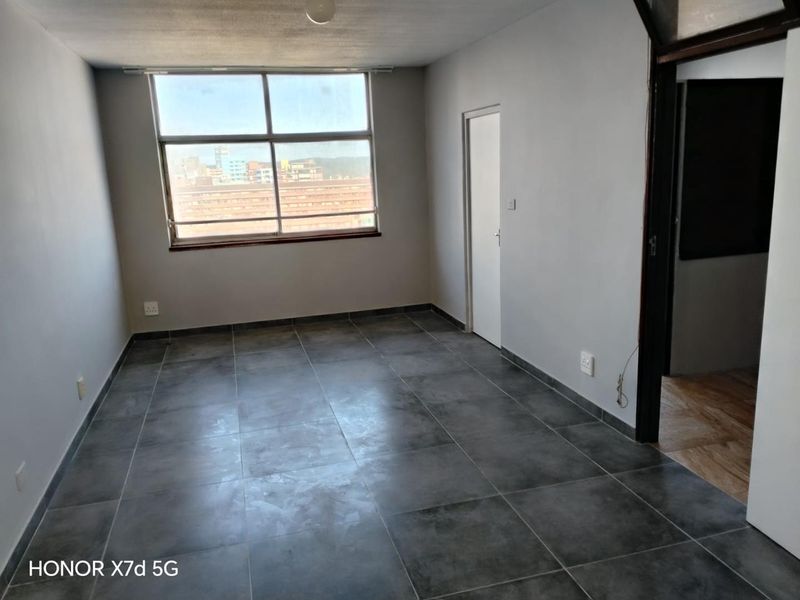 An empty living room featuring large windows, grey tiled flooring, and neutral walls, offering a blank canvas for interior design and personalization.