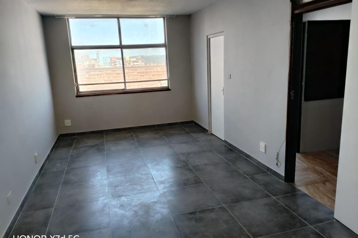 An empty living room featuring large windows, grey tiled flooring, and neutral walls, offering a blank canvas for interior design and personalization.