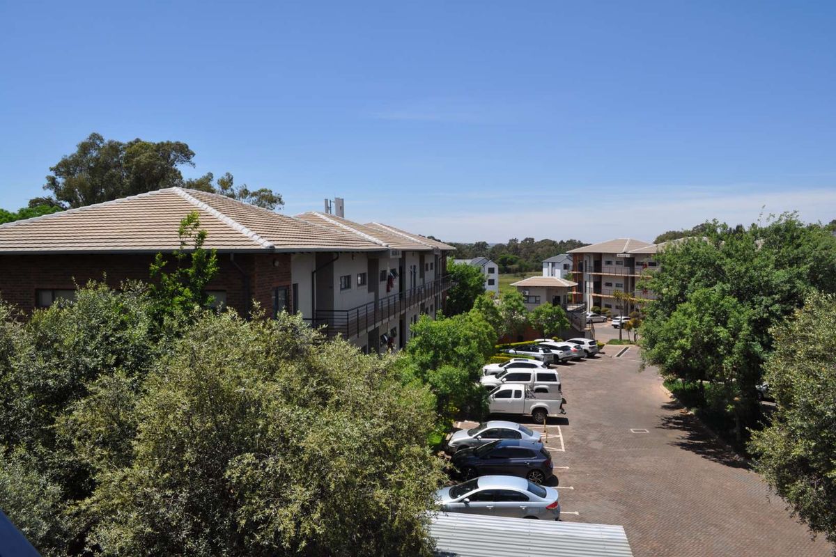 An elevated view of the office complex grounds, featuring multi-story buildings with tiled roofs and an extensive paved parking area surrounded by mature trees.
