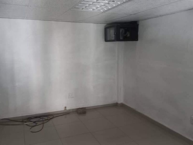 An empty office space featuring tiled flooring, a suspended ceiling, and a wall-mounted network cabinet, requiring minor cosmetic updates.