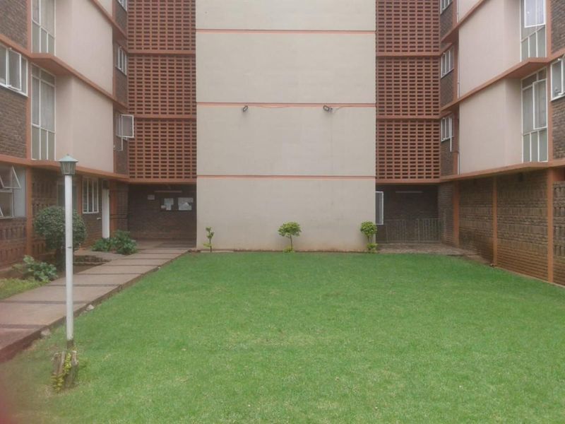 A communal courtyard area featuring a central lawn, paved walkways, and brick apartment building facades with decorative breeze block ventilation screens.