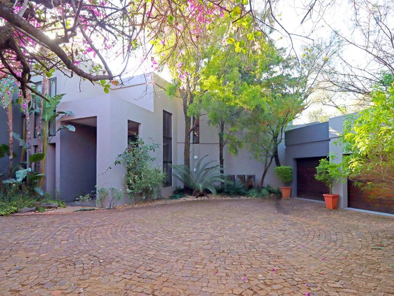 Front elevation of a modern farm-style residence featuring a circular cobblestone driveway, mature landscaping, and a double garage.