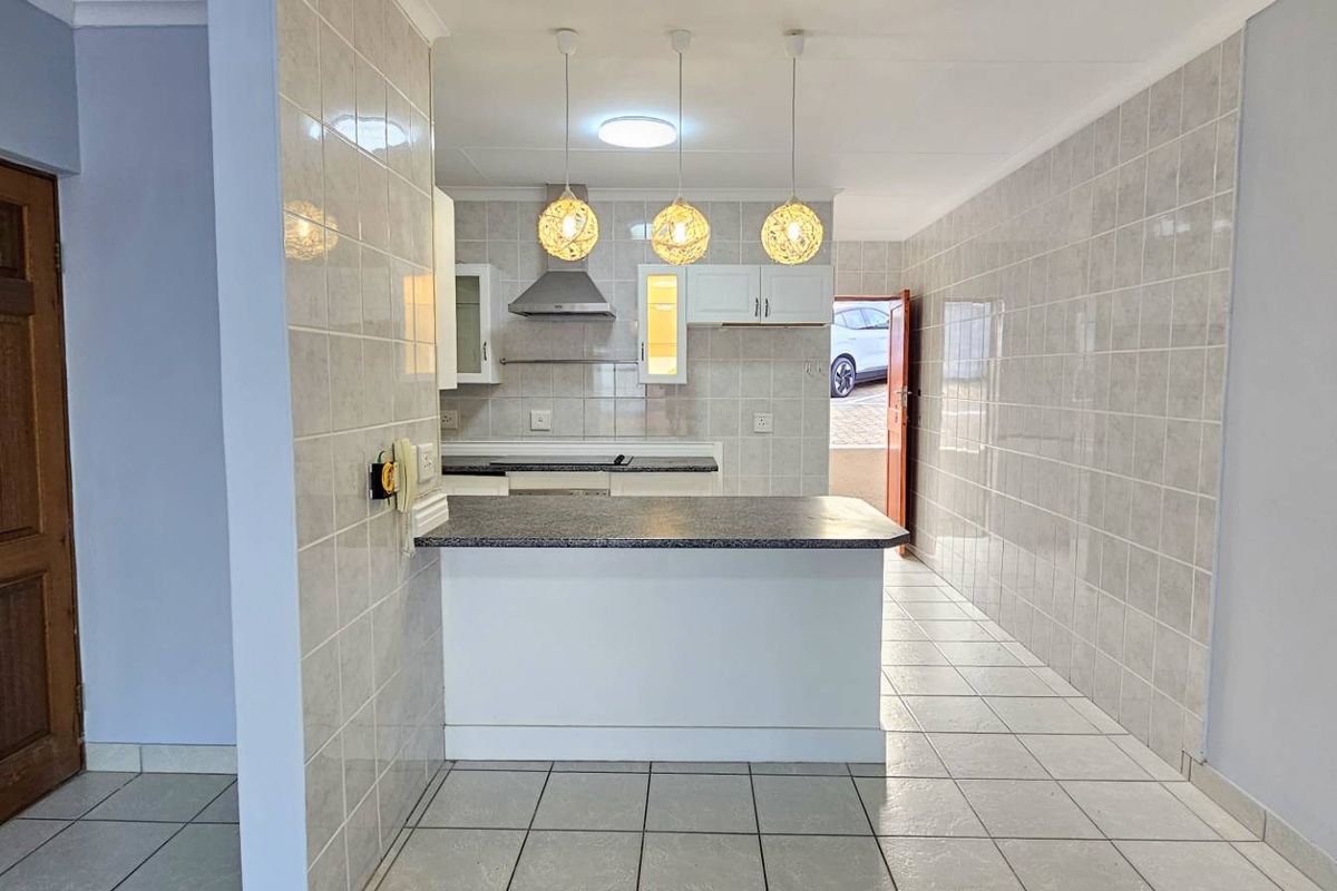 A functional kitchen featuring a breakfast bar, tiled walls, built-in cabinetry, and a stainless steel extractor fan, leading directly to an exterior entrance.