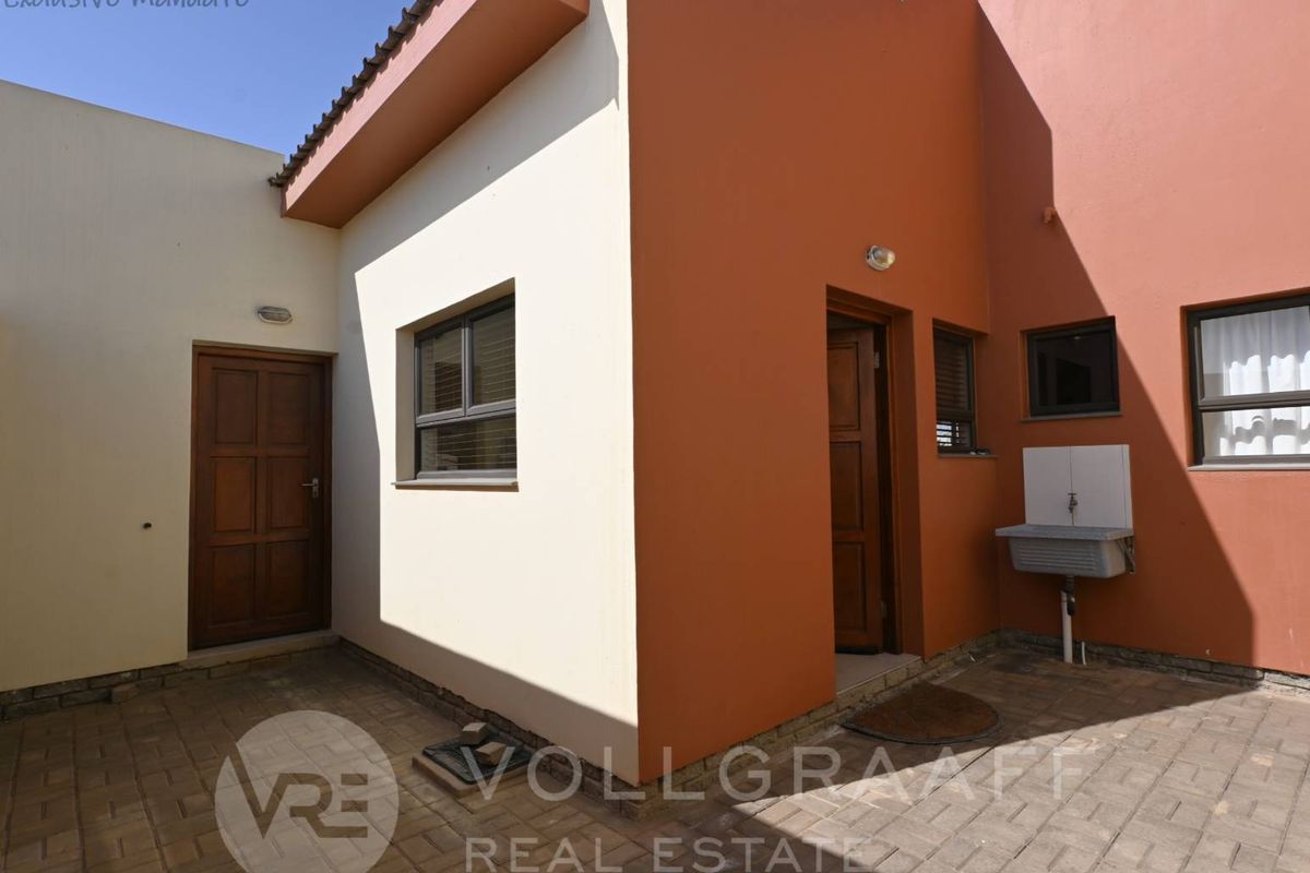 A paved rear courtyard area featuring exterior access doors, a utility sink, and painted masonry walls.